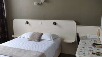 Een hotelkamer met een bed, nachtkastje met een lamp, een stoel en een klein bureau met stoel.