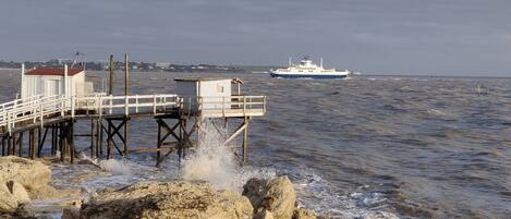 A pier with a lifeguard station and a small building, extending into a body of water with a boat in the distance.