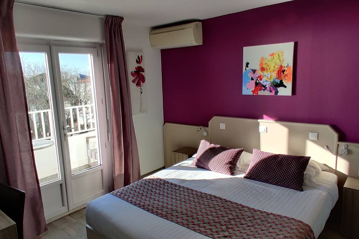 A bedroom with a bed, a desk, and a window with curtains.