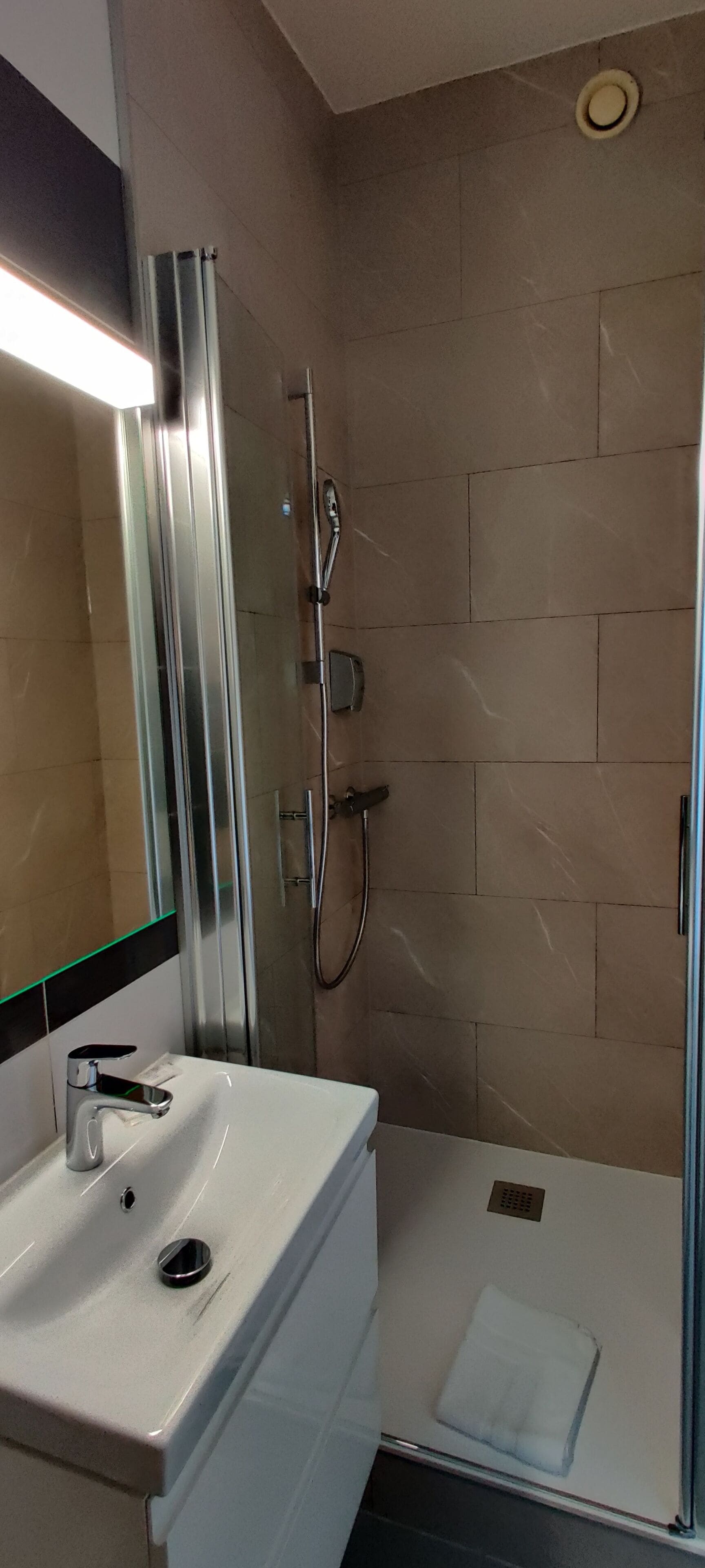 A modern bathroom with a glass-enclosed shower, a white sink, and a mirror with a green light strip.
