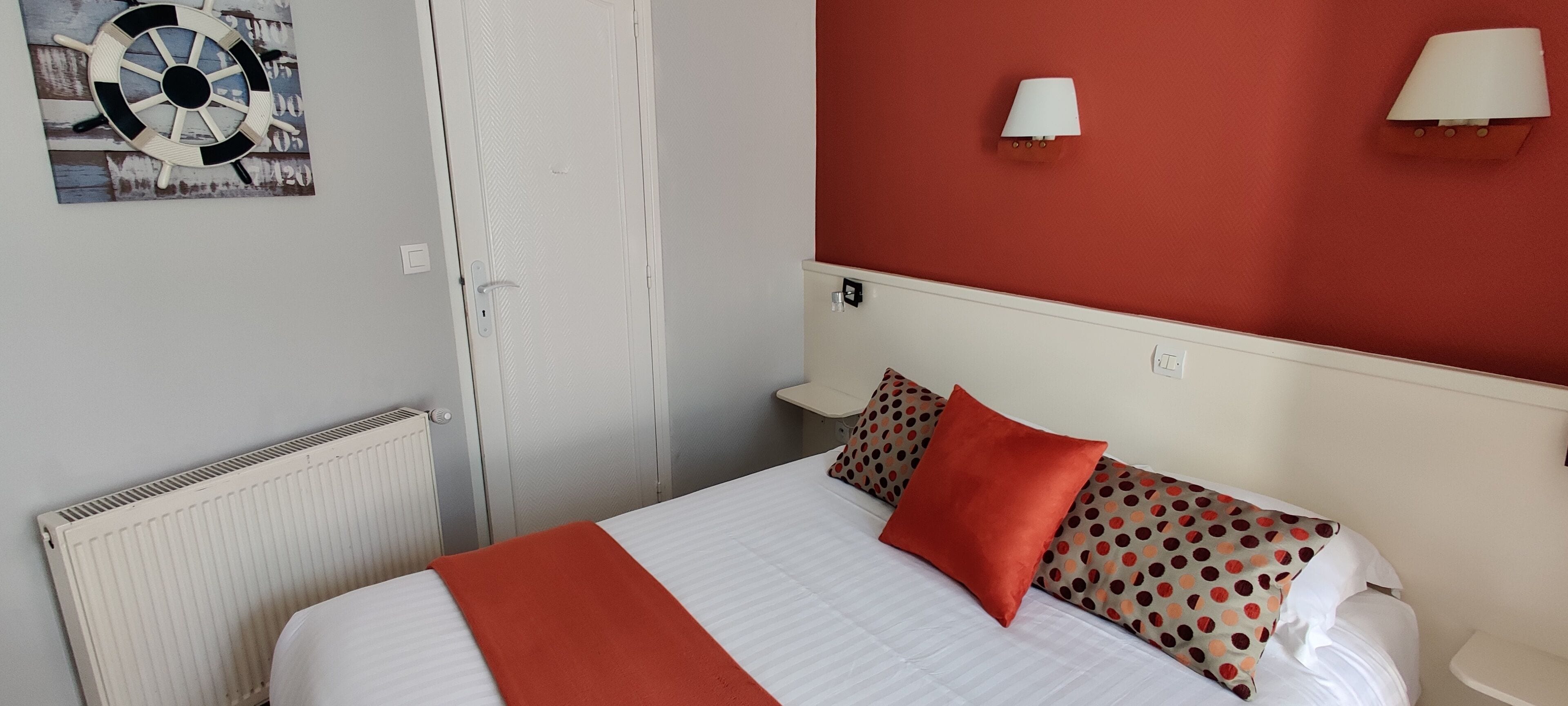 Une chambre d’hôtel avec un lit, un radiateur, une porte et un mur orné d’une roue décorative et de deux lampes murales.