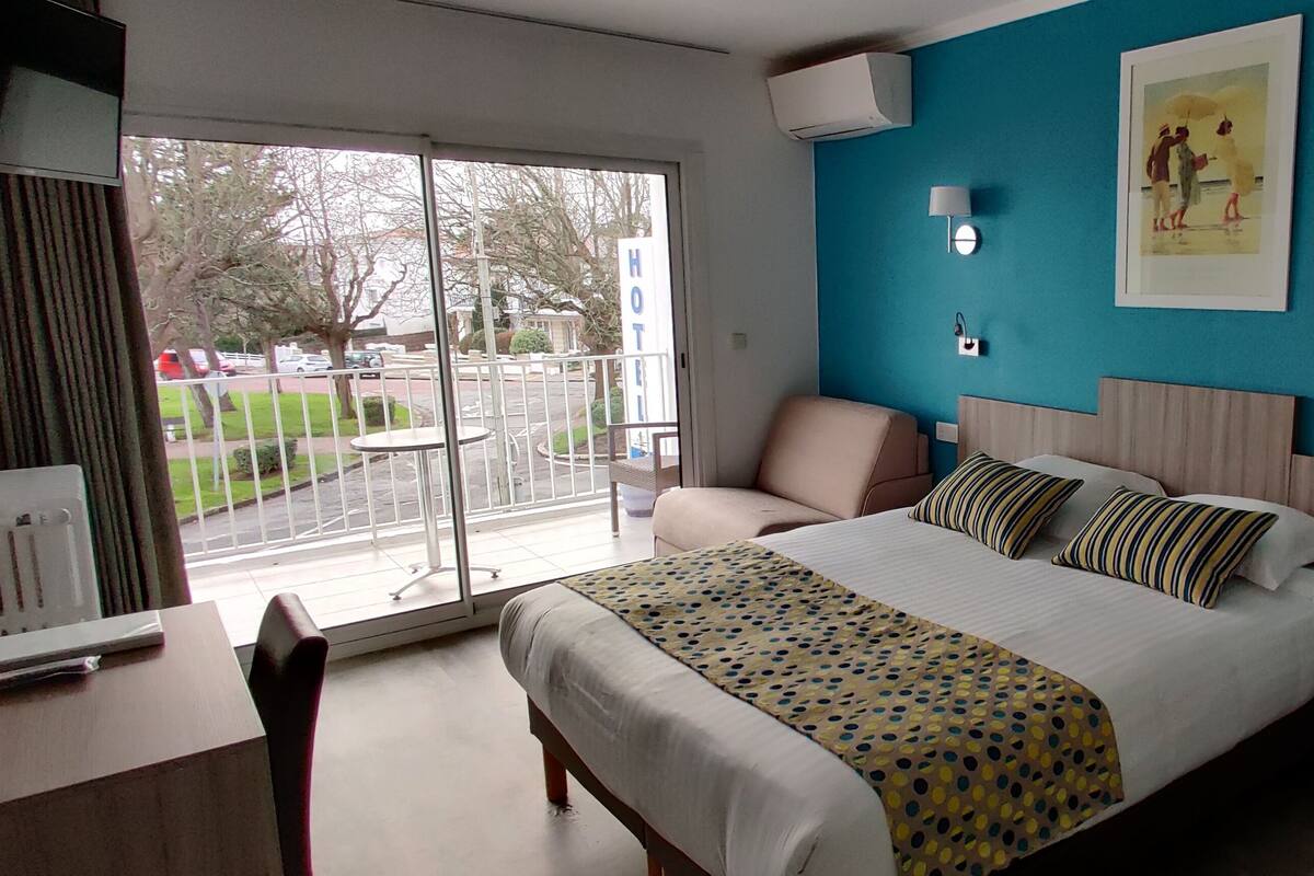 A hotel room with a bed, bedside tables, a chair, a desk, and a large window with a view of the outside.