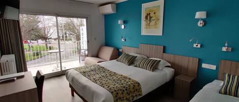 A hotel room with a bed, bedside tables, a chair, a desk, and a large window with a view of the outside.
