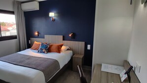 A hotel room with a bed, a nightstand, a lamp, and a window with curtains. - Logis Hotel Les Bleuets (Royan)