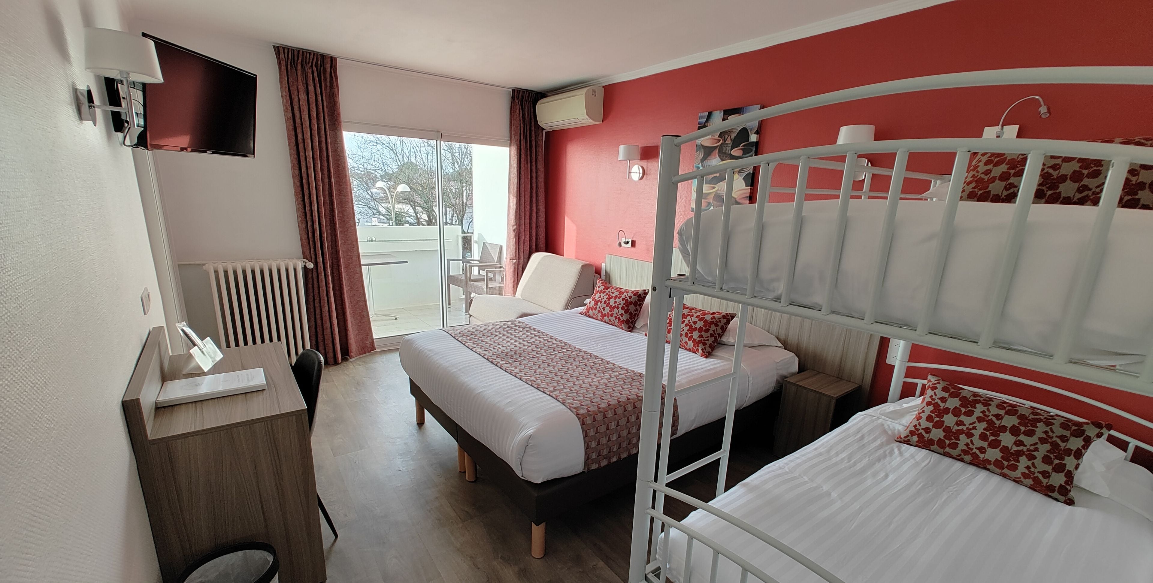 Quarto de hotel com duas camas, uma escrivaninha, uma cadeira, um radiador e vista para o exterior.