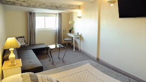 Une chambre d’hôtel avec un lit, un bureau, une chaise, une lampe et une fenêtre.