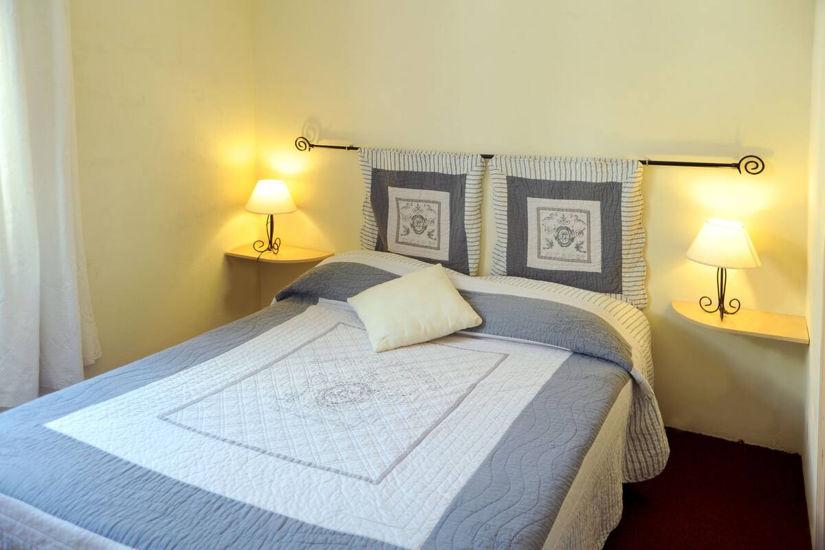 A neatly made bed with a quilt and pillows, two wall-mounted lamps, and a decorative headboard.