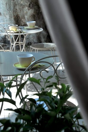 Un patio con mesas y sillas de metal, algunas con tazas y platillos.