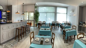 Un restaurante con manteles azules, sillas de madera y una zona de bar con un reloj y una máquina de café.