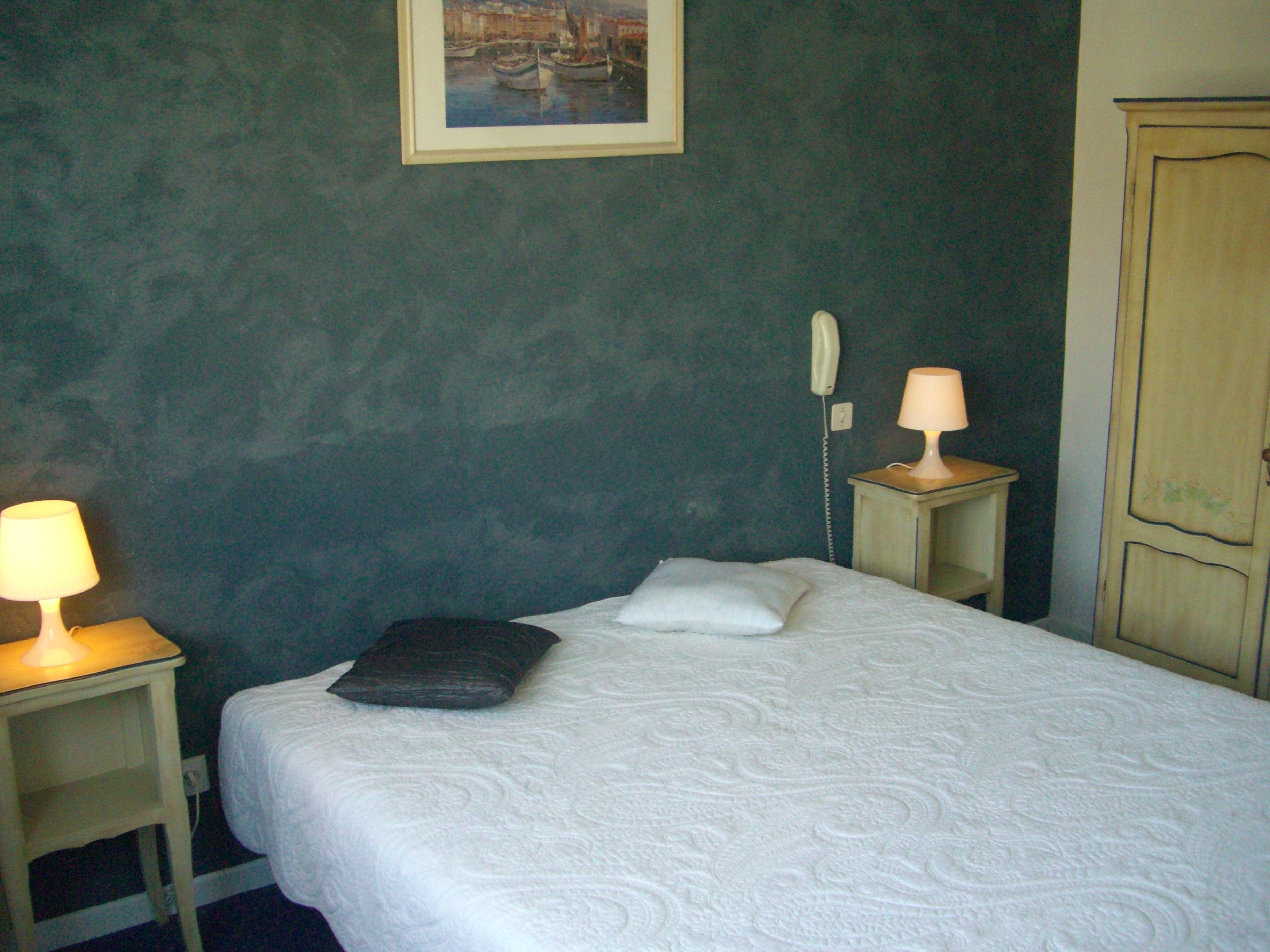 A room with a bed, a bedside lamp, a telephone, and a painting on the wall.