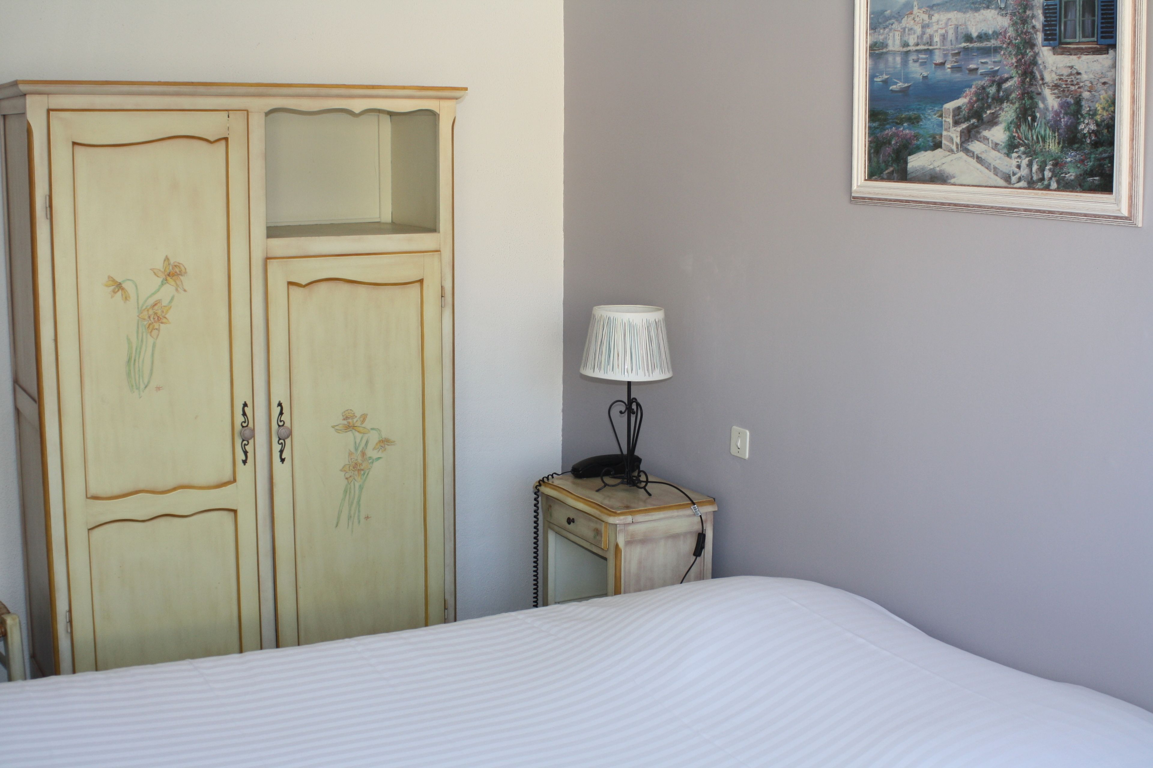 A bedroom with a bed, a wardrobe, a bedside table with a lamp, and a painting on the wall.