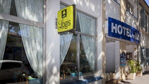 Un hotel con un cartel de 'Logis' y un cartel que dice 'HOTEL', ventanas grandes con cortinas y un toldo azul.