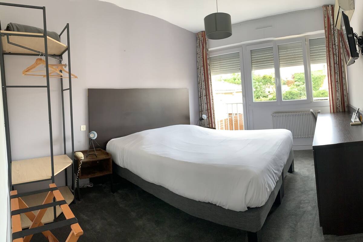A bedroom with a bed, a desk, a wardrobe, and a window with curtains.