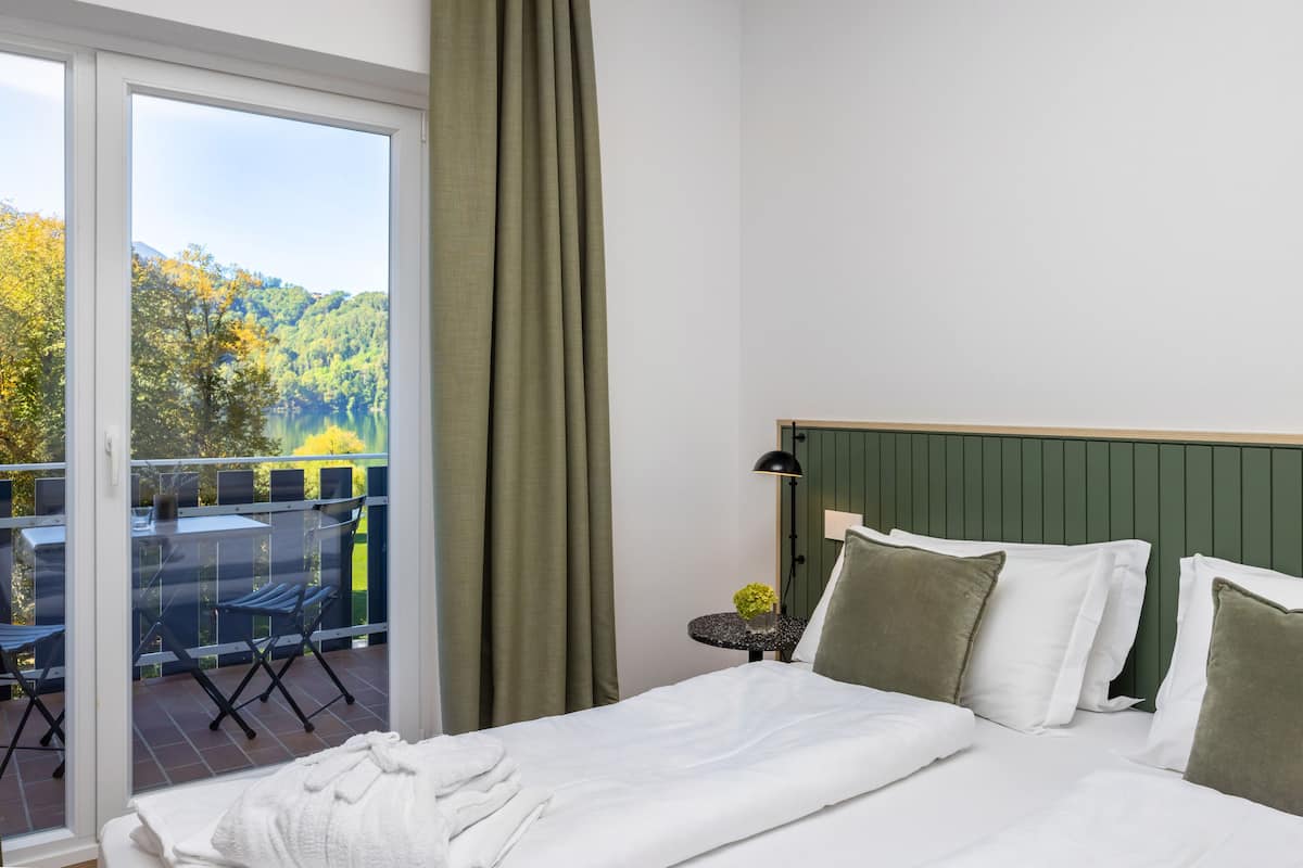 Een hotelkamer met een bed, een kleine tafel met een plant en uitzicht op een balkon met tuinmeubilair.