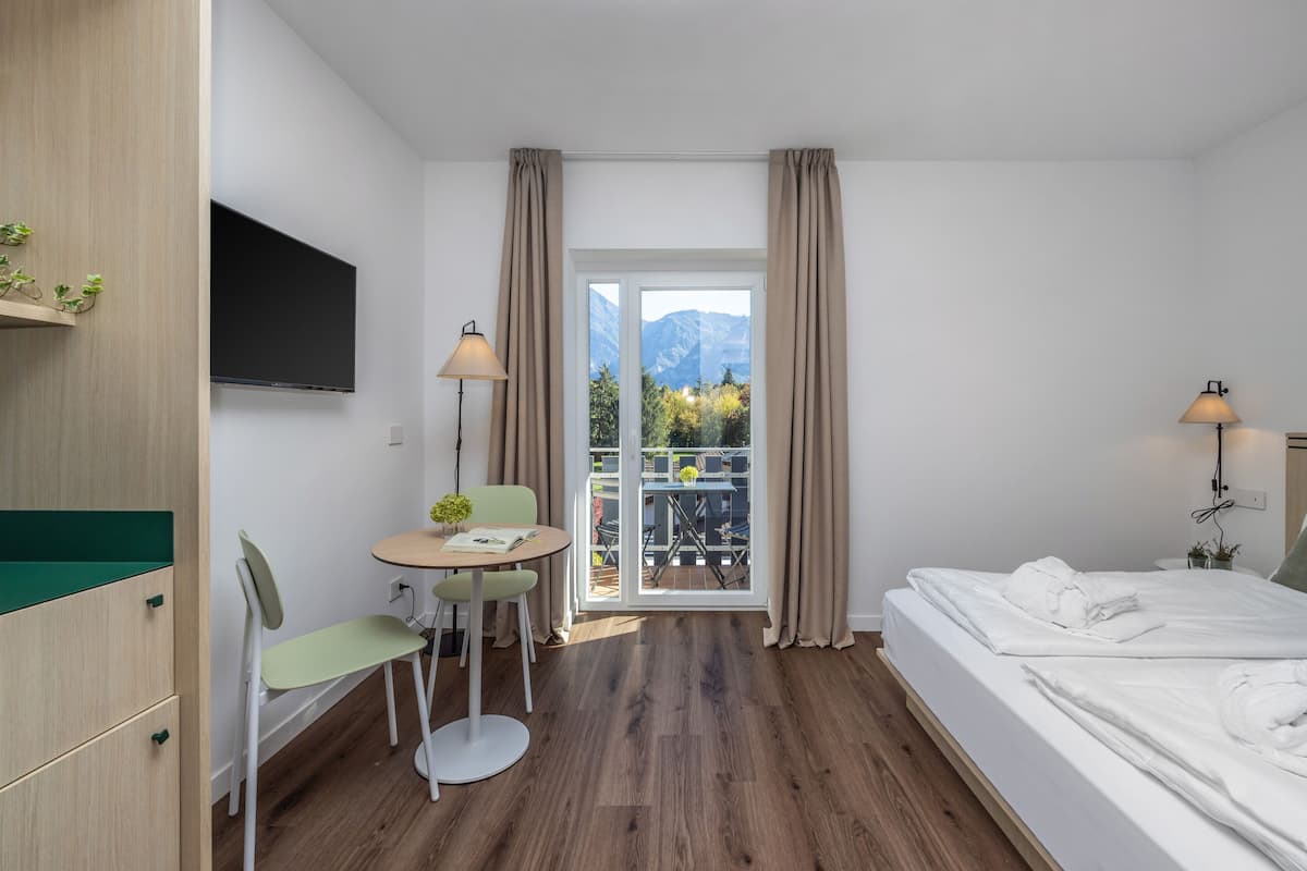 Een hotelkamer met een bed, een bureau met stoel, een televisie en een balkon met gordijnen.