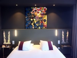 Quarto de hotel com uma cama grande, duas mesas de cabeceira e uma obra de arte pendurada na parede.