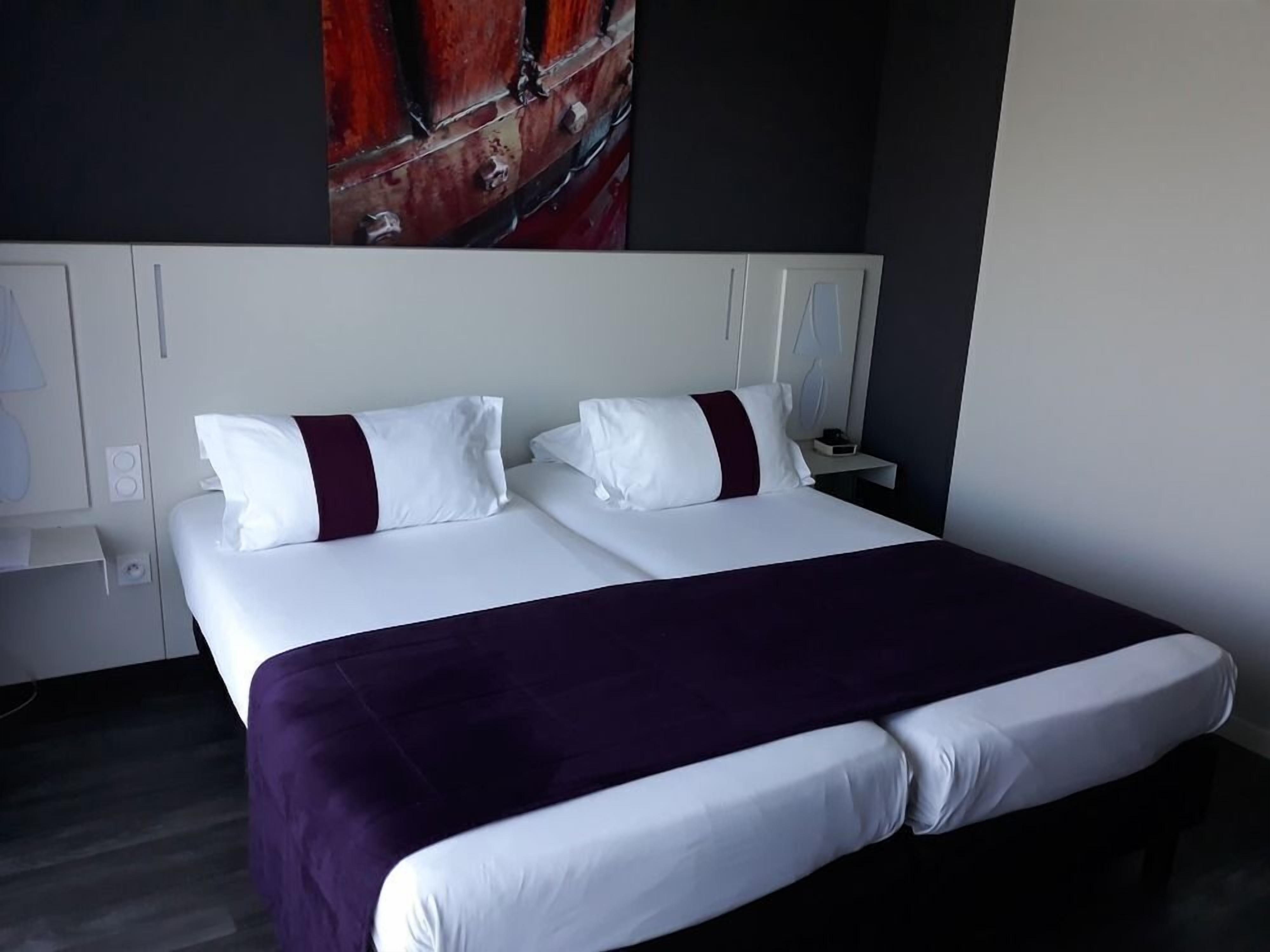 A hotel room with a large bed, white bedding, and a purple throw blanket.