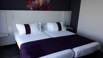 Una habitación de hotel con una cama grande, ropa de cama blanca y una manta morada.