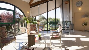 Un balcón amplio con vista a árboles y una piscina, amueblado con sillas y una mesa, y un reloj en la pared.