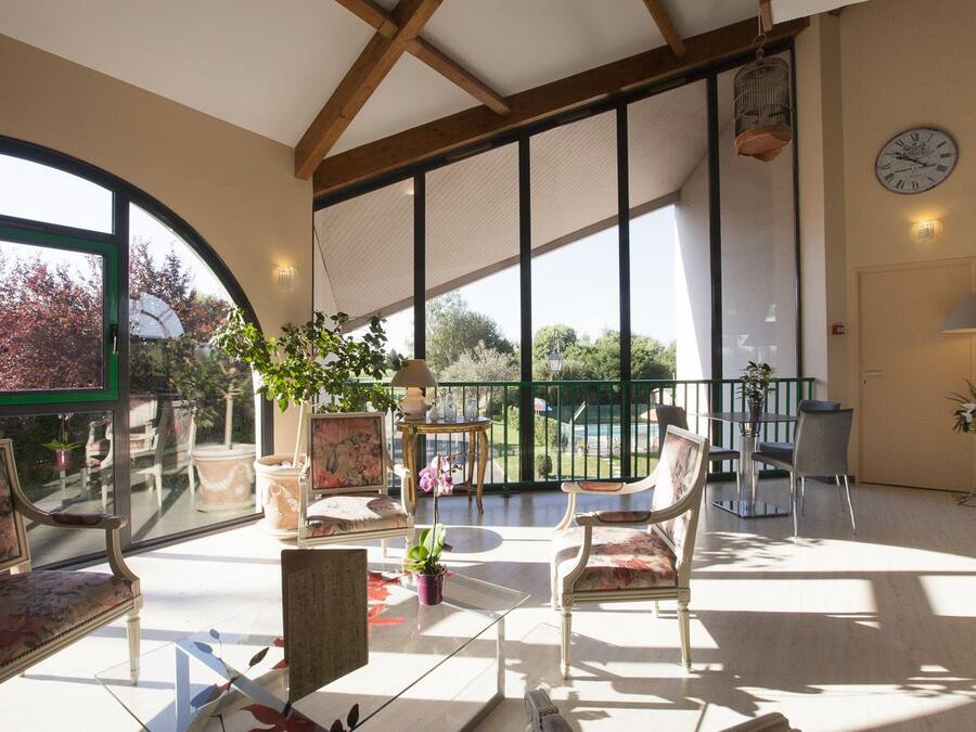 Ein geräumiger Balkon mit Blick auf Bäume und einen Pool, ausgestattet mit Stühlen und einem Tisch, und einer Uhr an der Wand.
