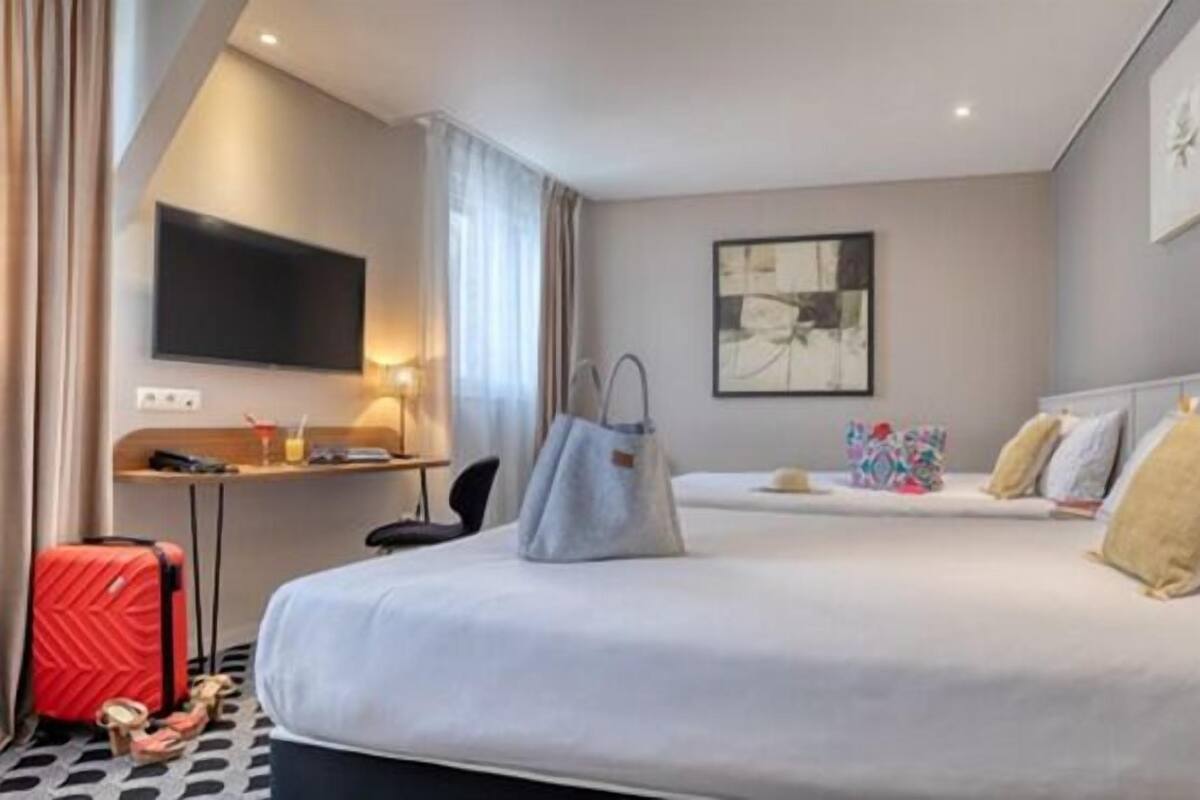 A hotel room with a large bed, a desk with a computer, a TV, and a painting on the wall.