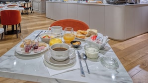 Ein Frühstücksbuffet mit verschiedenen Speisen und Getränken, eine Sitzgelegenheit mit Tischen und Stühlen sowie eine Theke mit einer Kaffeemaschine.