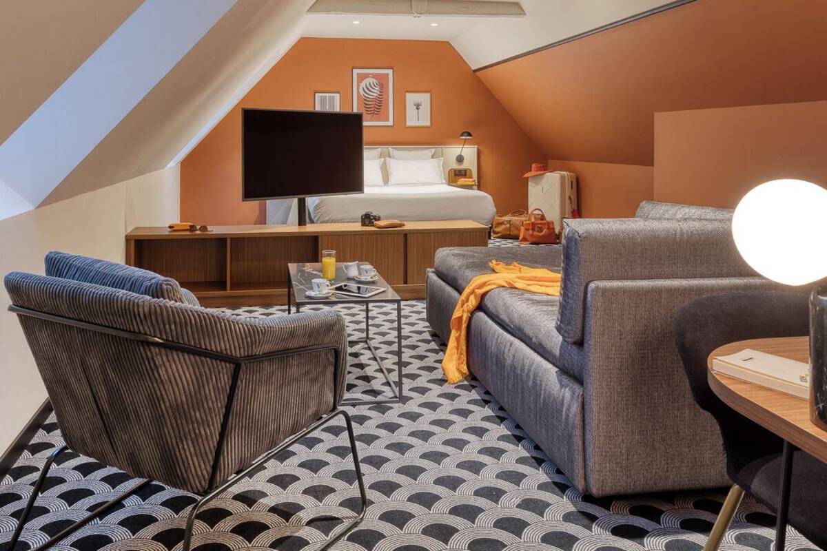 A modern, compact room with a loft-style ceiling, a bed, a desk, a TV, and seating areas.