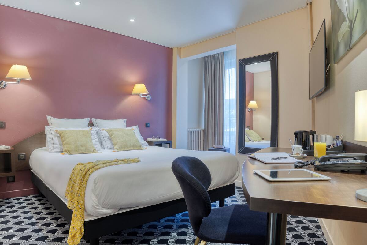 A hotel room with a bed, bedside lamps, a desk with a computer, and a mirror.