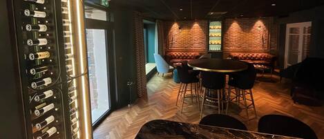 Un espace bar doté d’un comptoir en marbre, de sièges en cuir et d’une étagère où sont exposées des bouteilles.