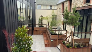 Ein moderner Innenhof mit Holzdeck, Pflanzgefäßen und einem Steinhaus.