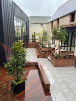 A modern courtyard with a wooden deck, planters, and a stone building.