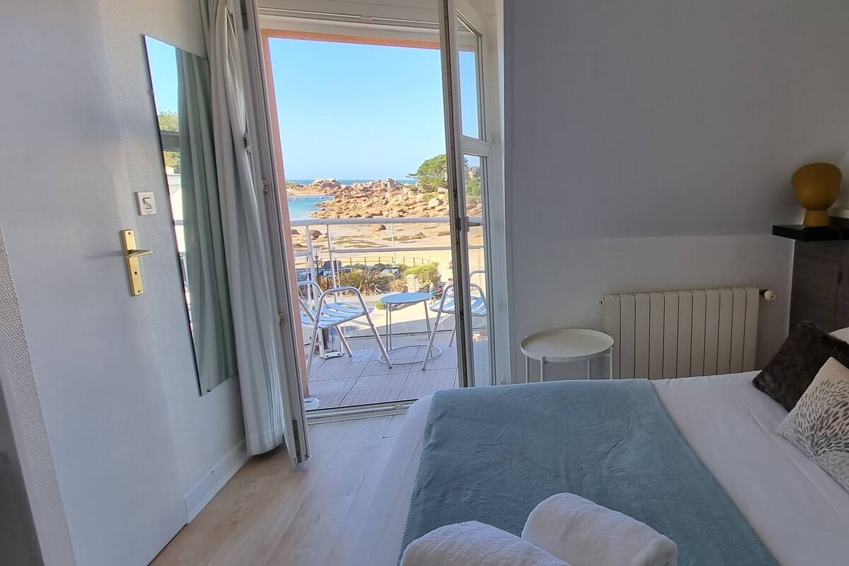 Ein Schlafzimmer mit Bett, einem kleinen Tisch, einem Sessel und Blick auf den Strand.