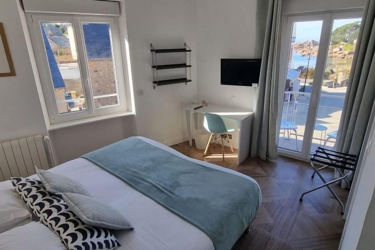 Un dormitorio con cama, escritorio, televisor y vistas al exterior.