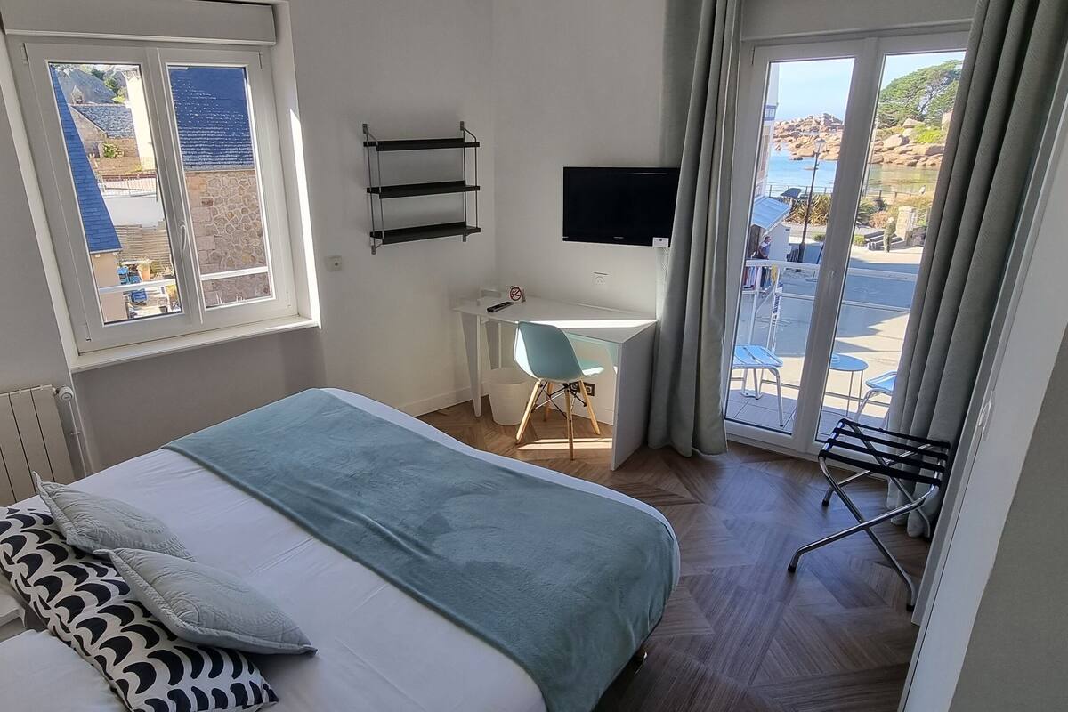 Ein Schlafzimmer mit Bett, Schreibtisch, Stuhl, Fernseher und einem Fenster mit Meerblick.