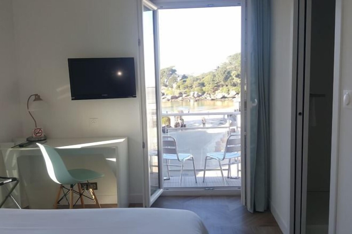 Una habitación de hotel con cama, escritorio con silla, televisión y balcón con mesa y sillas.