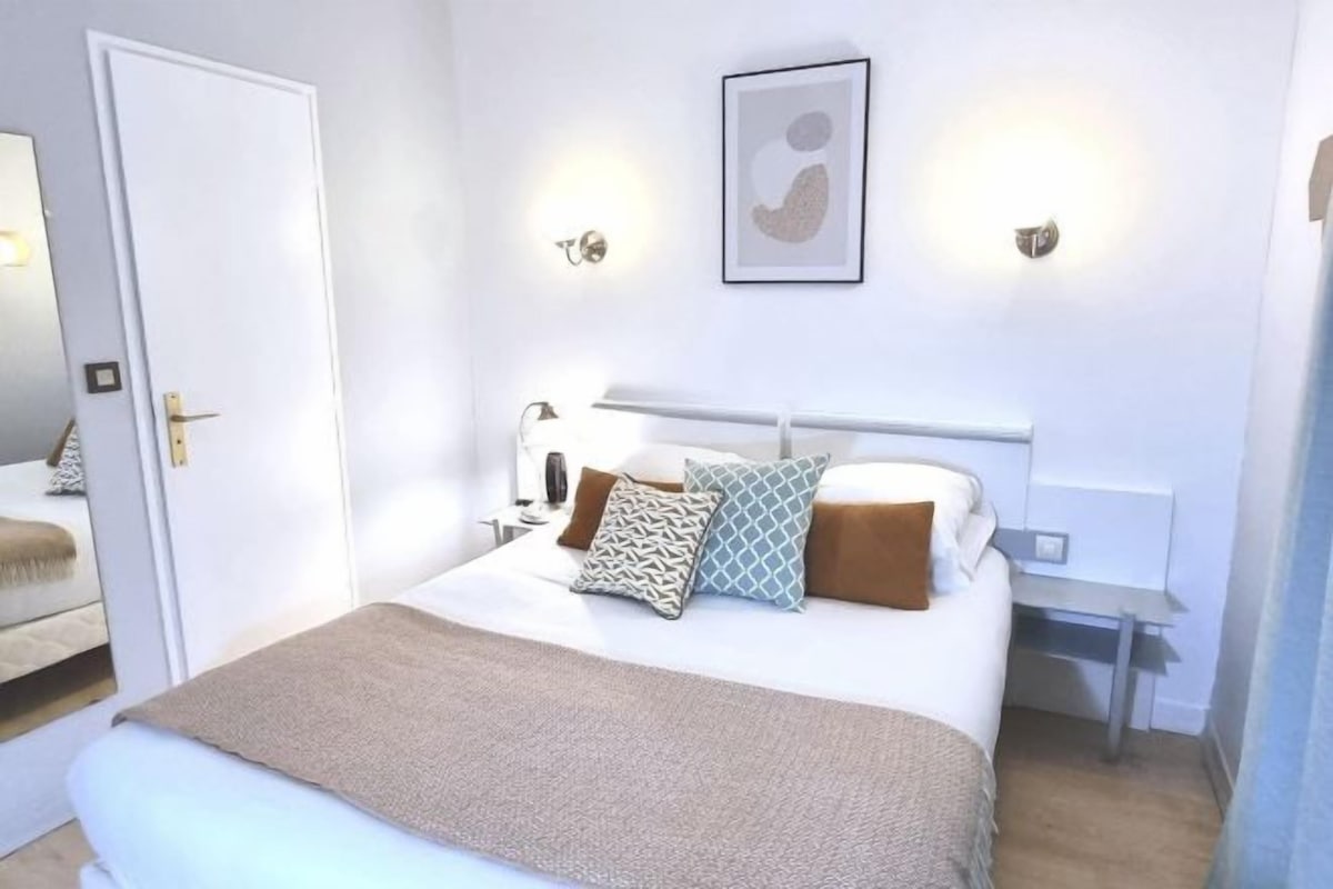 Un dormitorio ordenado con cama, mesitas de noche y una lámpara fijada a la pared.