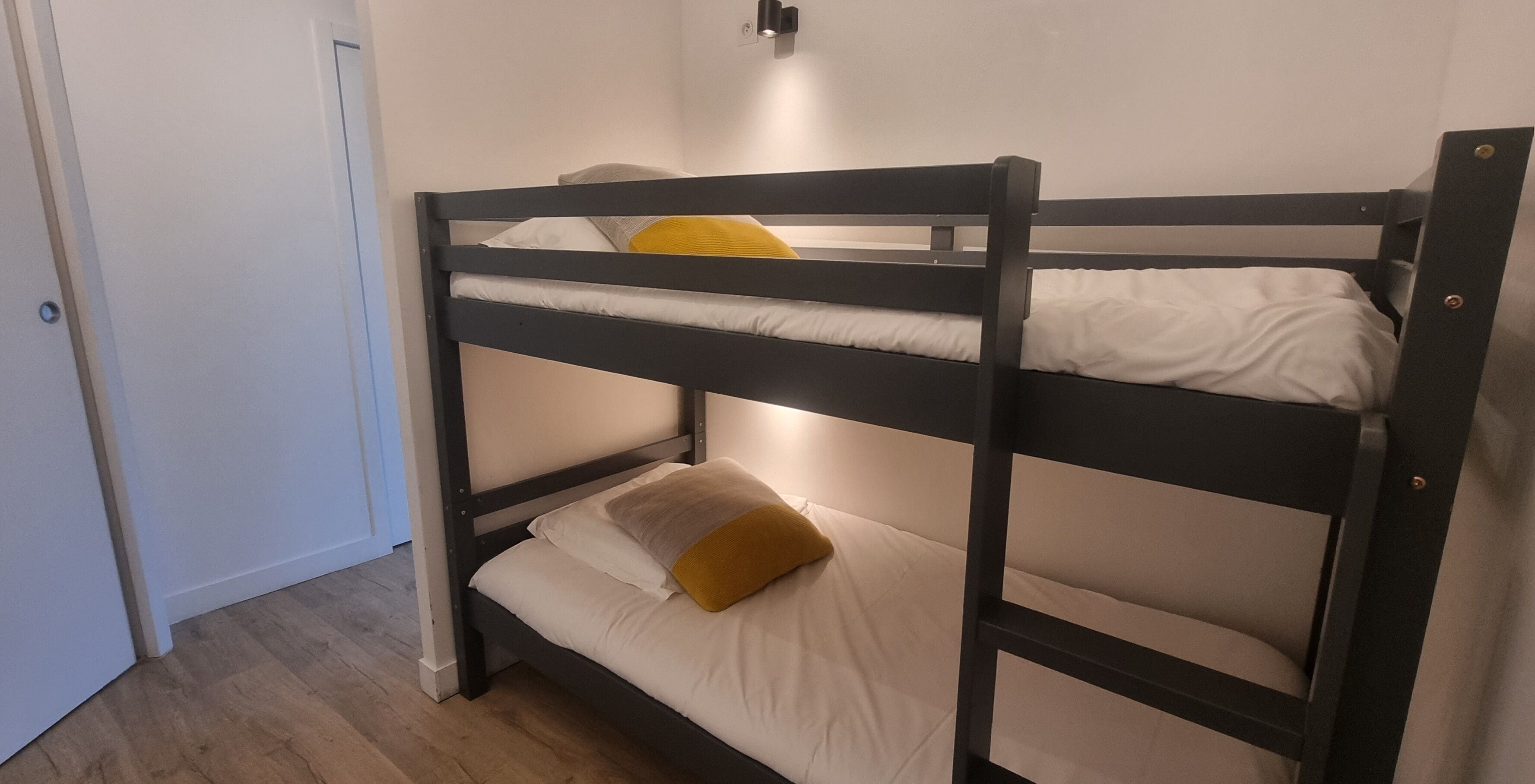 A bunk bed with two levels, a door to the left, and a light fixture above the bed.