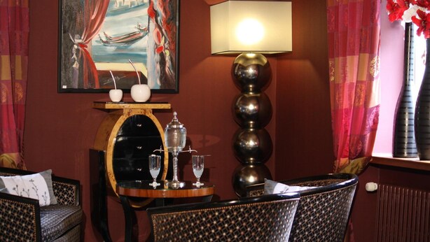 A dining area with a table set for two, a lamp, and a painting of a river scene. - Hôtel Taillard (Goumois)