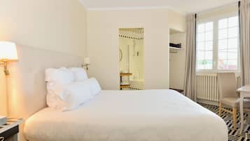 Een hotelkamer met een groot bed, een nachtkastje, een lamp, een raam met gordijnen en een badkamer zichtbaar door een geopende deur.
