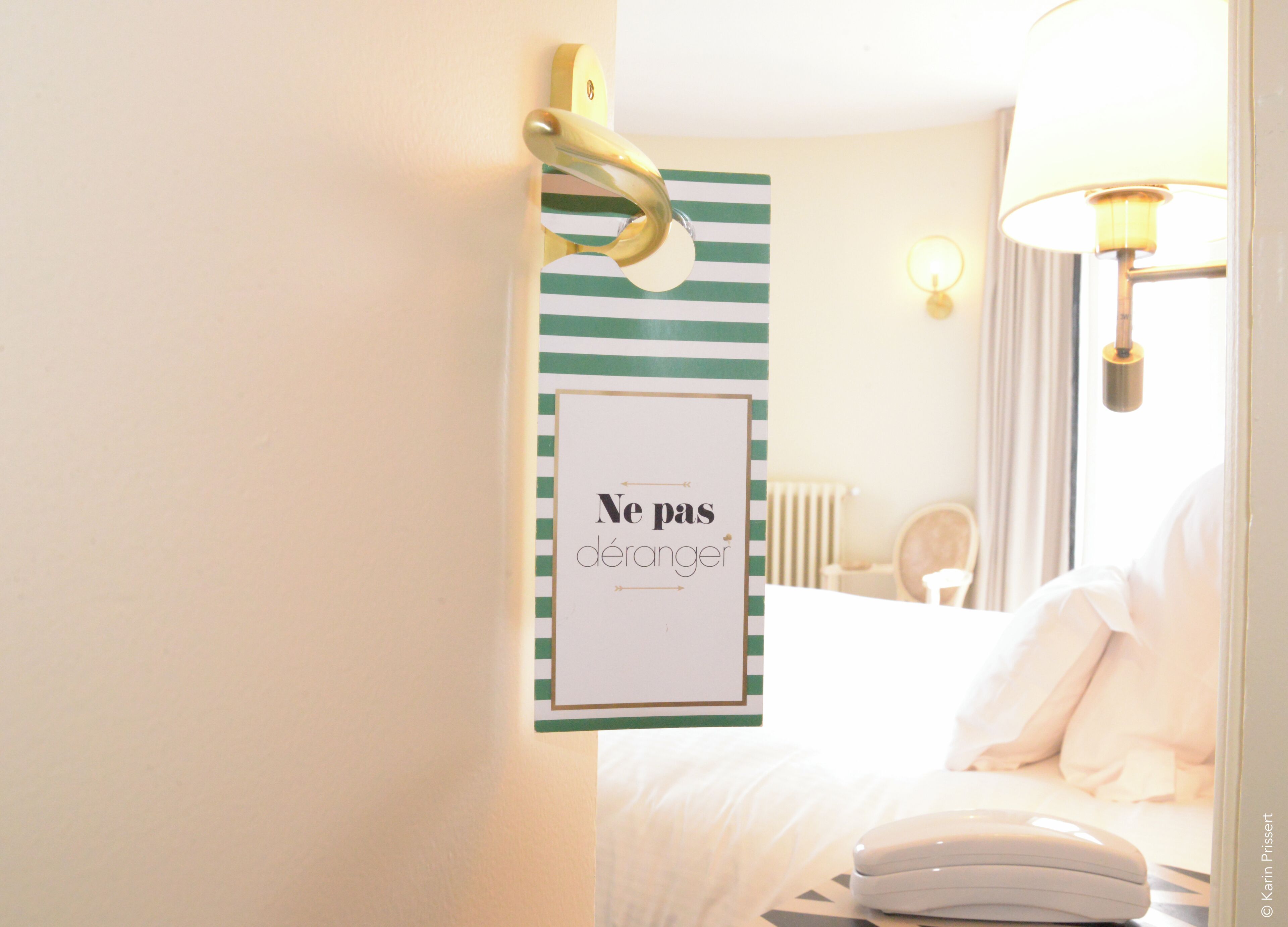 A hotel room with a bed, a bedside table, a lamp, and a sign on the wall.