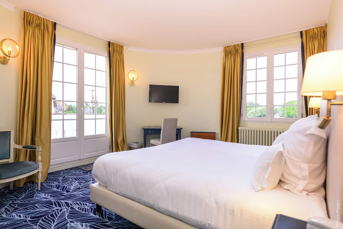 A hotel room with a large bed, a desk, a chair, a TV, and a window with curtains.