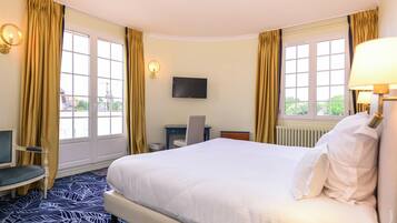 A hotel room with a large bed, a desk, a chair, a TV, and a window with curtains.