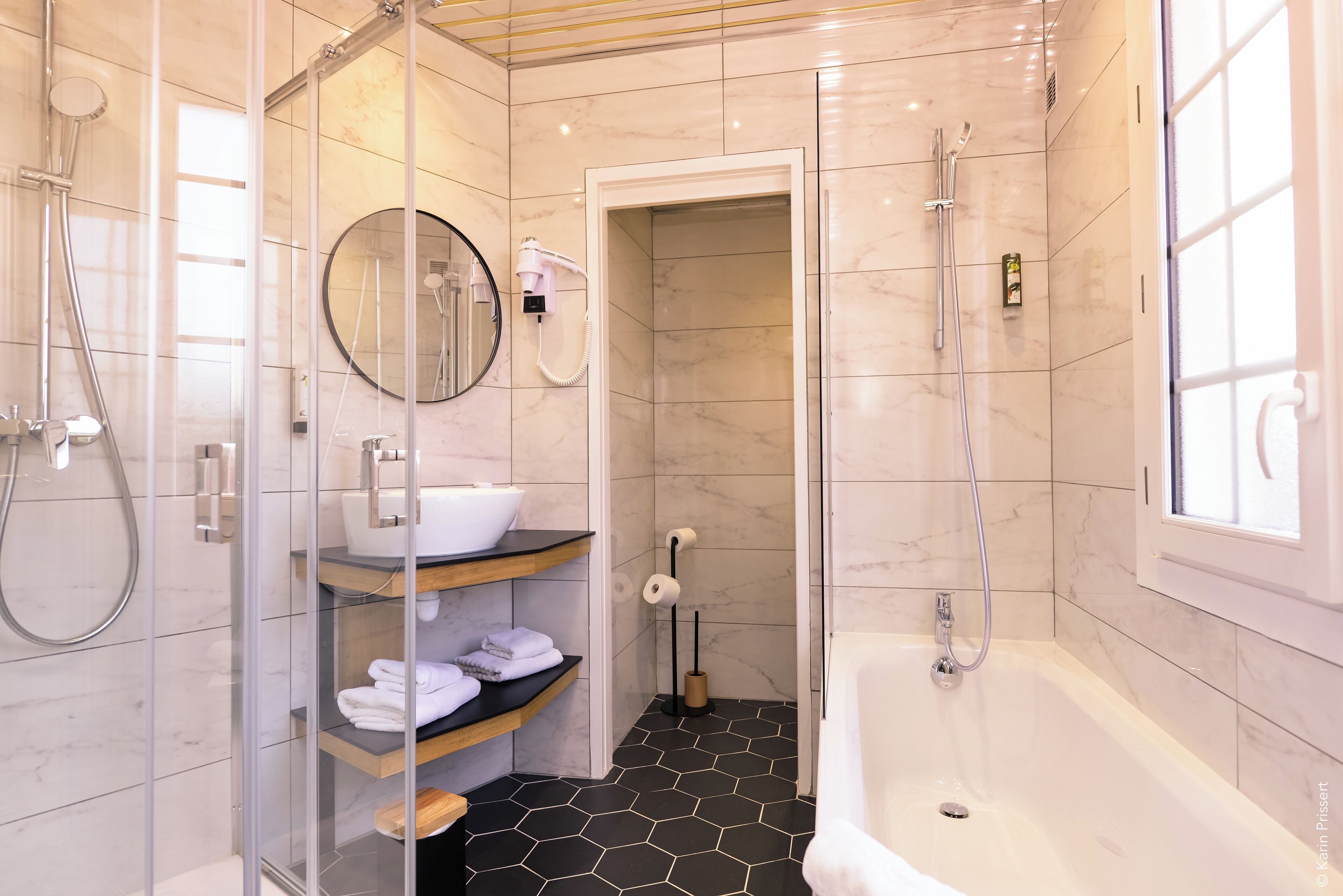 Une salle de bain moderne dotée d’une douche à parois de verre, d’une baignoire blanche et d’un meuble-lavabo avec un évier et des étagères.