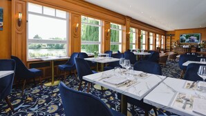 Un restaurante con mesas largas, ventanas amplias y vistas a zonas verdes.