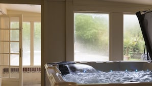 A hot tub with water flowing, a door leading outside, and a view of greenery through a window.