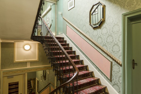A grand staircase with ornate railings and patterned wallpaper.