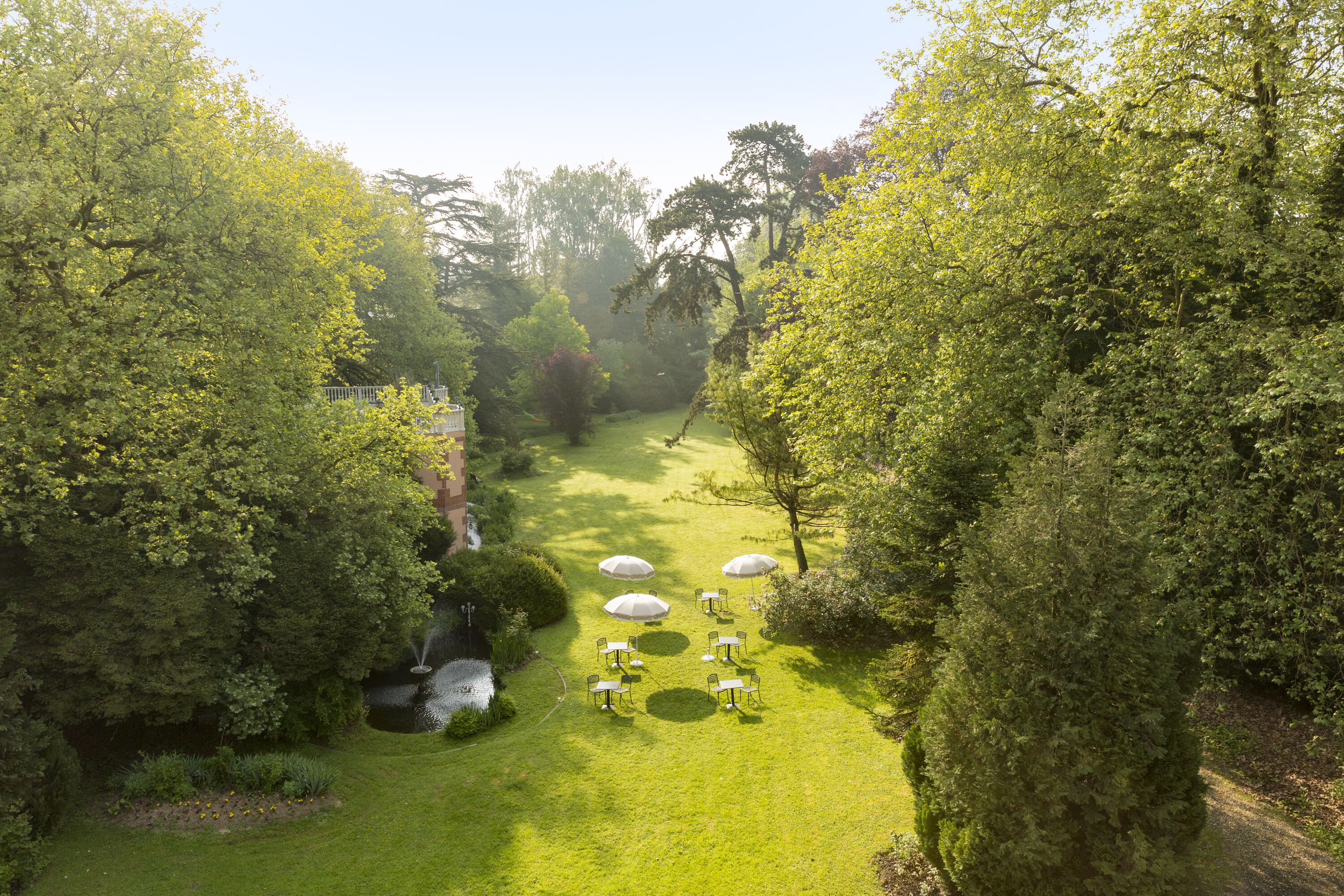 Luchtbeeld van een weelderige tuin met een pad, omringd door dichte begroeiing en verschillende tafels met parasols.