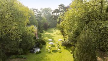 Luchtbeeld van een weelderige tuin met een pad, omringd door dichte begroeiing en verschillende tafels met parasols.