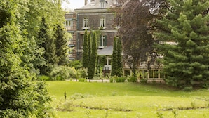 A large, historic building with multiple stories, surrounded by lush greenery and a well-maintained garden.