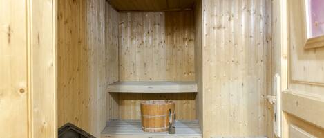 Eine Holzsauna mit einer Holzbank, einem Eimer und einem Steinberg.